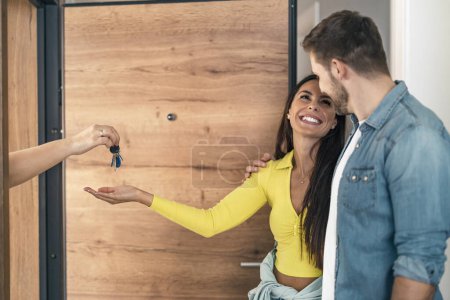 Téléchargez les photos : Jeune femme tenant les clés de la maison tout en embrassant le mari dans leur nouvel appartement après l'achat de biens immobiliers. - en image libre de droit