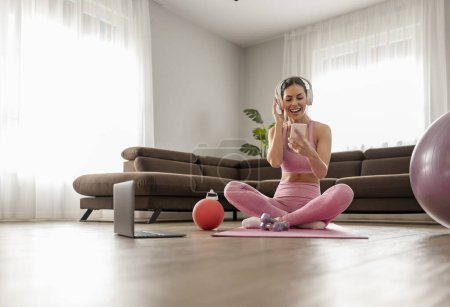Téléchargez les photos : Jeune femme après l'exercice à la maison écouter de la musique sur les écouteurs. Exercice à domicile. - en image libre de droit