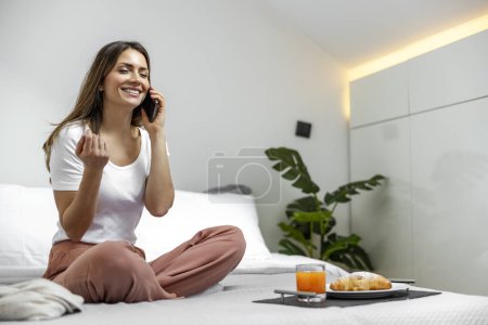 Foto de Mujer joven feliz utilizando el teléfono inteligente en el hogar.Ella está en el dormitorio. - Imagen libre de derechos