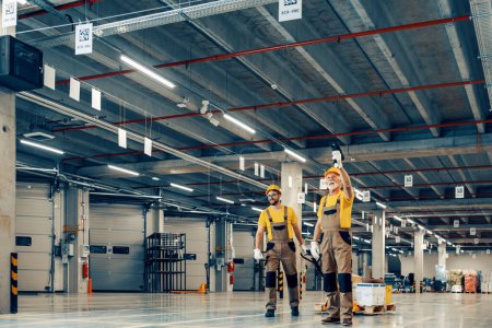 Photo for Two workers in uniform at warehouse.Warehouse workers pulling a pallet truck.Warehouse. - Royalty Free Image