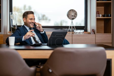 Foto de Joven hombre de negocios hablando por teléfono y utilizando el ordenador portátil mientras está sentado en su lugar de trabajo. Concepto de empresa, personas y tecnología. - Imagen libre de derechos