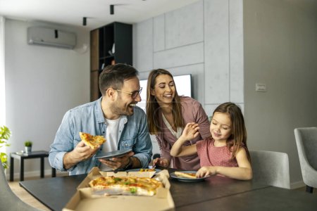 Photo for Mom, dad and daughter are eating together at home. Happy family eating pizza at home. - Royalty Free Image