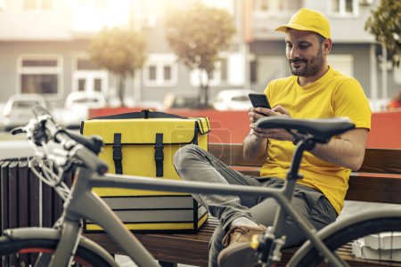 Foto de Repartidor sonriente con bolsa térmica y bicicleta en la calle de la ciudad.Entrega de alimentos a los clientes. - Imagen libre de derechos