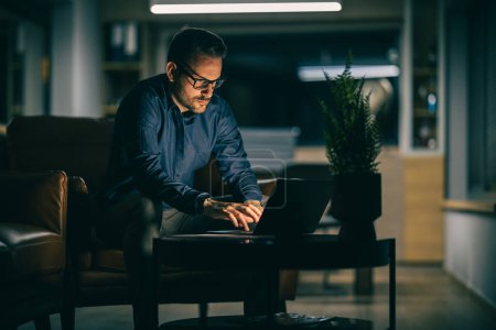 Téléchargez les photos : Homme d'affaires sérieux travaillant sur ordinateur portable la nuit dans un bureau moderne.Homme d'affaires fatigué et inquiet sur le lieu de travail. - en image libre de droit