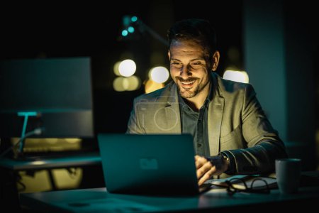 Téléchargez les photos : Portrait d'un bel homme d'affaires travaillant sur ordinateur au bureau tard dans la soirée. Homme d'affaires travaillant tard dans la nuit au bureau avec ordinateur portable. - en image libre de droit