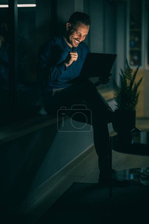 Téléchargez les photos : Jeune homme d'affaires assis dans la chaise de sac et utilisant la tablette numérique après la journée réussie sur le travail.Célébrer le succès. - en image libre de droit