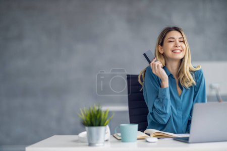 Téléchargez les photos : Jeune femme assise à une table dans le bureau avec ordinateur portable, travaillant à partir du bureau moderne. Achats en ligne. - en image libre de droit