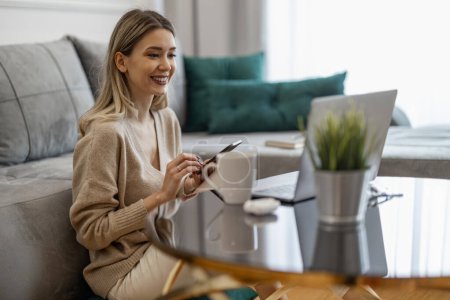 Foto de Atractiva joven con ropa casual usando laptop mientras trabaja en casa.Mujer sonriente freelancer trabajando en casa. - Imagen libre de derechos