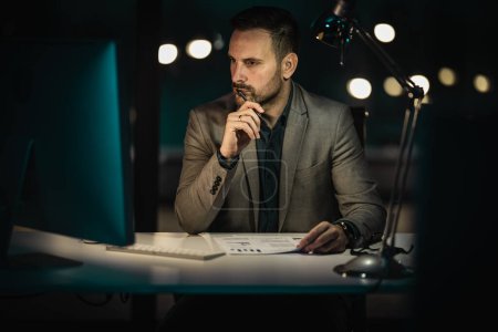Téléchargez les photos : Portrait d'un bel homme d'affaires travaillant sur ordinateur au bureau tard dans la soirée. Homme d'affaires travaillant tard dans la nuit au bureau avec ordinateur. - en image libre de droit
