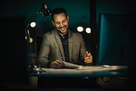 Foto de Retrato de un hombre de negocios guapo trabajando en la computadora en la oficina a última hora de la noche. Empresario trabajando hasta tarde en la noche en la oficina con el ordenador. - Imagen libre de derechos