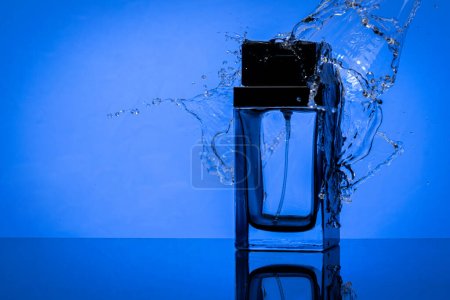 Foto de Botella de perfume y salpicaduras de agua a su alrededor, sobre fondo azul. Burla de frasco de perfume - Imagen libre de derechos