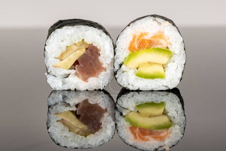 Téléchargez les photos : Deux rouleaux de sushi au saumon, thon et avocat. Sushi avec réflexion. Nourriture japonaise traditionnelle - en image libre de droit