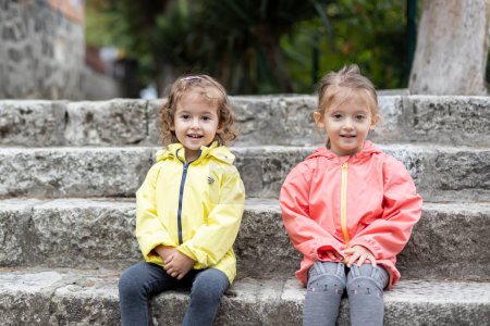 Téléchargez les photos : Two little girls sitting on the stairs, outside. Happy childhood - en image libre de droit