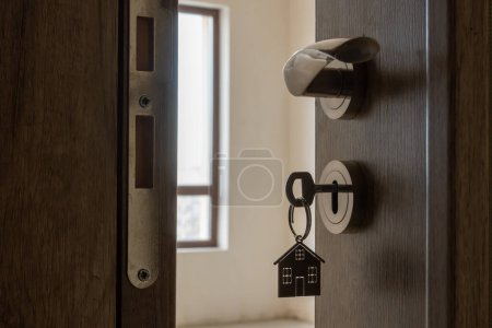 Photo for Open door to a new home. Door handle with key and home shaped keychain. Mortgage, investment, real estate, property and new home concept - Royalty Free Image
