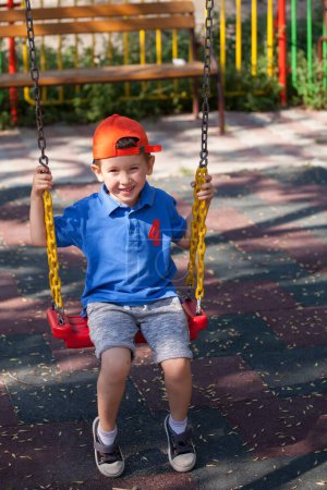 Foto de Feliz niño balanceándose en el columpio de cadena. Zona de juegos al aire libre
. - Imagen libre de derechos