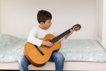 Foto de Niño aprendiendo a tocar la guitarra acústica. Niño está practicando la guitarra acústica en su habitación - Imagen libre de derechos