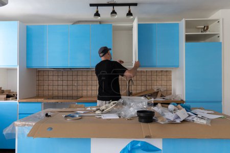 Téléchargez les photos : Charpentier travaillant sur une nouvelle cuisine. bricoleur fixer une porte dans une cuisine - en image libre de droit