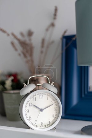 Photo for White alarm clock on bed table in bedroom. - Royalty Free Image