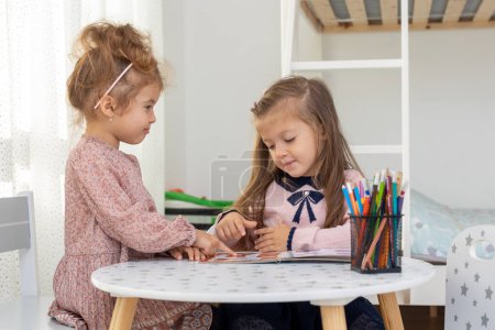 Photo for Cute children girls are reading a book in room at home. Two sister girls reading a book and having fun. - Royalty Free Image