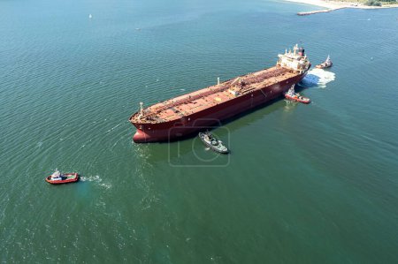 Foto de Vista aérea del remolcador asistiendo al gran petrolero. Gran buque petrolero entra en el puerto escoltado por remolcadores. - Imagen libre de derechos