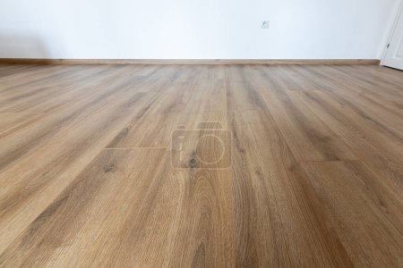 Photo for Laminated wood floor with white wall. Empty room with floating laminate in new apartmen - Royalty Free Image
