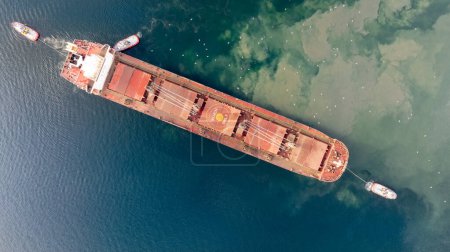 Photo for Aerial top down view of Tug boats assisting big cargo ship. Large cargo ship enters the port escorted by tugboats. - Royalty Free Image