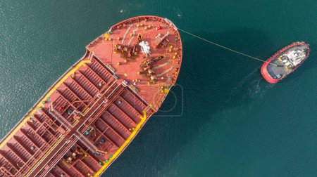 Téléchargez les photos : Vue aérienne du remorqueur qui assiste un gros pétrolier. Un grand pétrolier entre dans le port escorté par un remorqueur. - en image libre de droit