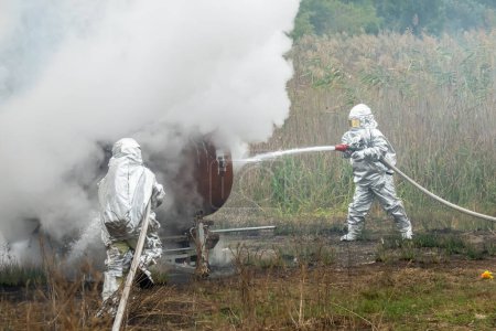 Foto de Dos bomberos con trajes de protección trabajan con manguera de agua. Luchando por un ataque de fuego - Imagen libre de derechos
