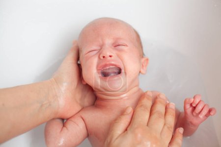 Foto de El bebé recién nacido está siendo bañado por su madre. Bebé recién nacido llorando en la hora del baño - Imagen libre de derechos