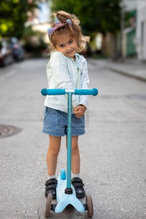 Téléchargez les photos : Joyeux petite fille jouer avec son scooter extérieur - en image libre de droit