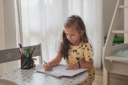 Foto de Cute little girl enjoys painting. Girl drawing and coloring picture with color pencil in her room at home - Imagen libre de derechos