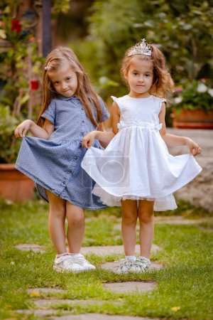 Foto de Lindos niños, retrato de niñas felices en vestidos de princesa. Dos hermanitas en un hermoso jardín - Imagen libre de derechos