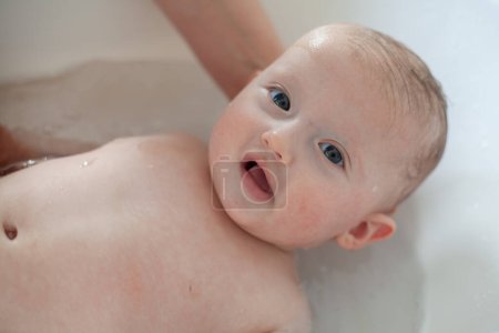 Téléchargez les photos : Le petit bébé est baigné par sa mère. Bébé mignon pendant le bain - en image libre de droit