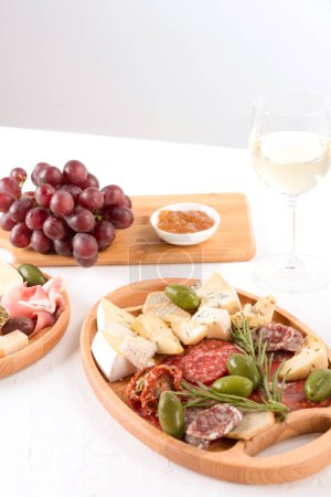 Photo for Charcuterie plate with different types of meat snacks - salami, bresaola, proscuitto. Wooden plates with traditional italian antipasti served with glass of white wine on white table - Royalty Free Image