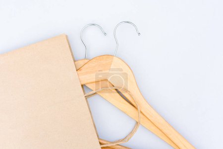 Green smart shopping concept. Paper bag with wooden hangers over light gray background with copy space. Slow fashion