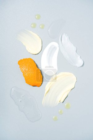 Muchas muestras de productos cosméticos con vitamina C - manchas de crema y gel, gotas de aceite sobre fondo gris claro. La crema mancha la textura. Antiaging productos para el cuidado de la piel con extracto cítrico y cáscara de naranja