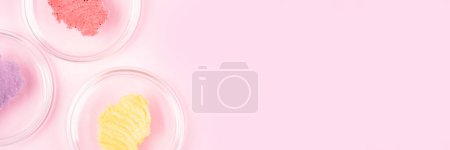 Foto de Scrub smudges in petri glass dishes over pastel pink background. Sugar body scrub smears. Long horizontal banner with copy space - Imagen libre de derechos