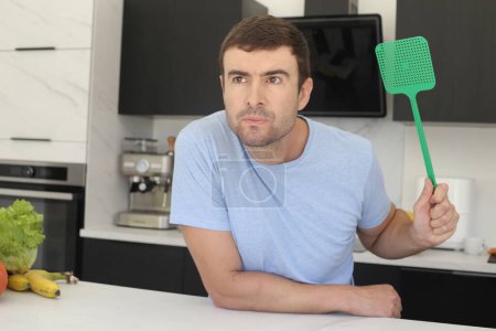 Photo for Portrait of handsome young man with fly swatter at kitchen - Royalty Free Image