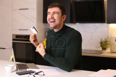 Photo for Portrait of handsome young man making e-shopping with credit card and laptop at kitchen - Royalty Free Image