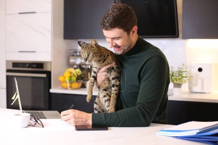 Photo for Portrait of handsome young man with his exotic cat sitting at kitchen - Royalty Free Image