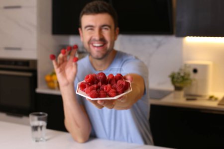 Photo for Portrait of handsome young man with raspberries at kitchen - Royalty Free Image