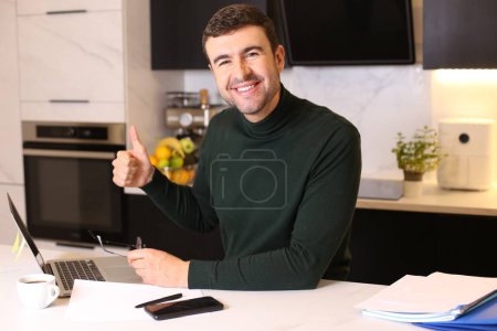 Foto de Retrato de joven guapo con portátil que trabaja desde casa en la cocina - Imagen libre de derechos