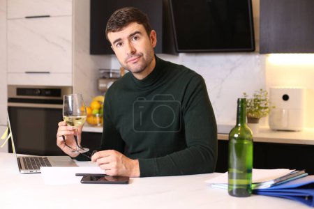 Foto de Retrato de joven guapo con copa de vino trabajando desde casa en la cocina - Imagen libre de derechos