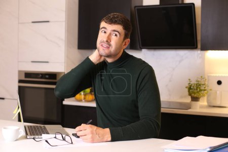 Téléchargez les photos : Portrait de beau jeune homme avec ordinateur portable travaillant de la maison à la cuisine - en image libre de droit