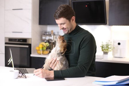 Téléchargez les photos : Portrait de beau jeune homme avec son petit chien mignon à la cuisine - en image libre de droit