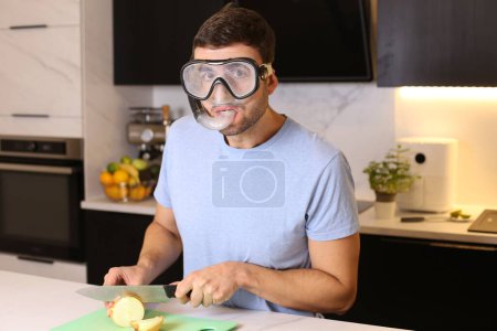 Foto de Retrato de joven guapo con máscara de snorkel cortando cebolla en la cocina - Imagen libre de derechos