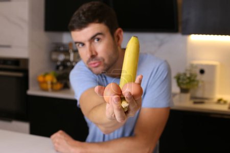 Foto de Retrato de joven guapo sosteniendo plátano en la cocina - Imagen libre de derechos