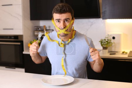 Photo for Portrait of handsome young man with head tied in measuring tape at kitchen, diet concept - Royalty Free Image