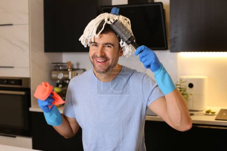 Téléchargez les photos : Portrait de beau jeune homme avec serpillière sur la tête à la cuisine - en image libre de droit