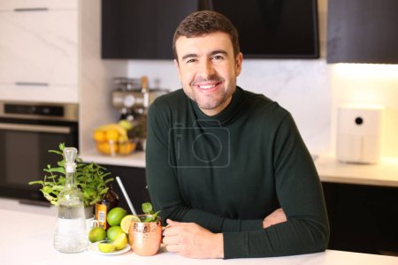Téléchargez les photos : Portrait de beau jeune homme avec limes et boisson à la menthe à la cuisine - en image libre de droit